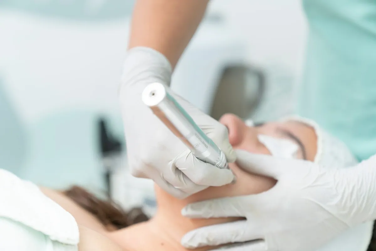 A gloved practitioner treating a patient's jawline with a pen-style skin device in a bright clinic room