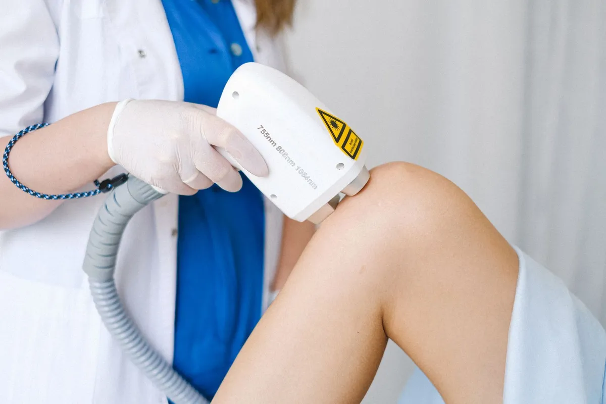 A gloved technician using a laser handpiece on a patient's leg
