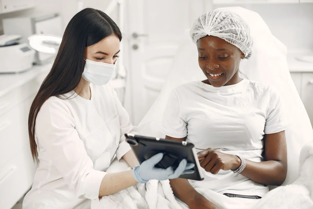 A masked practitioner going over skin photos on a tablet with a smiling patient