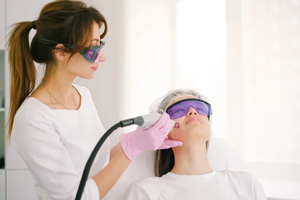 Elena Novak in laser goggles treating a patient's face with a laser handpiece