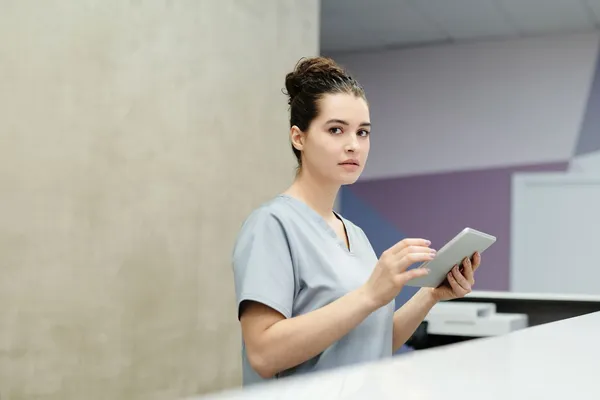 Jessica Hale in light blue scrubs holding a tablet at the clinic front desk